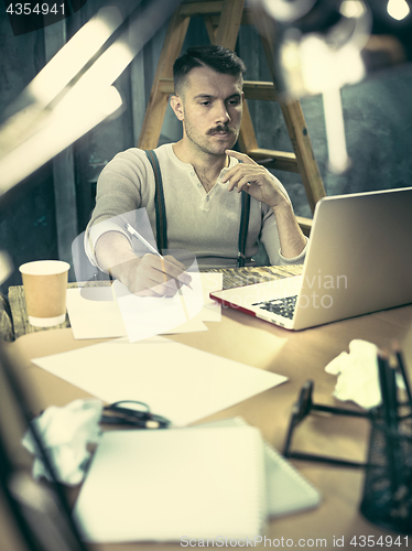 Image of Portrait of a bearded businessman who is checking details of his upcoming meeting in his notebook and typing.