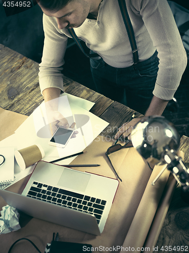 Image of Vintage hipster wooden desktop top view, male hands using a laptop and holding a pencil