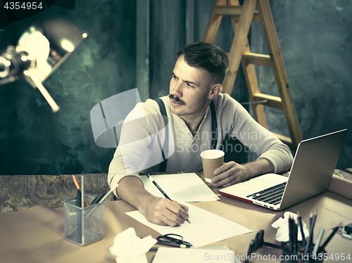 Image of Portrait of a bearded businessman who is checking details of his upcoming meeting in his notebook and typing.