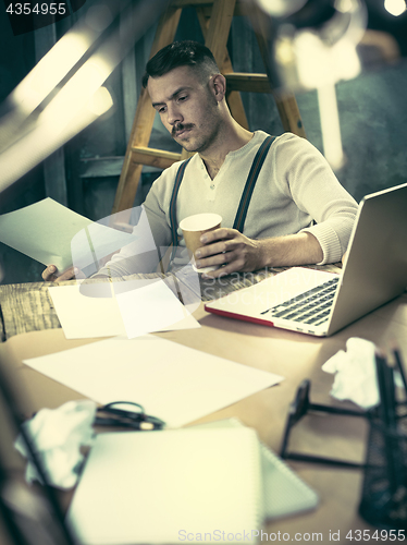 Image of Portrait of a bearded businessman who is checking details of his upcoming meeting in his notebook and typing.