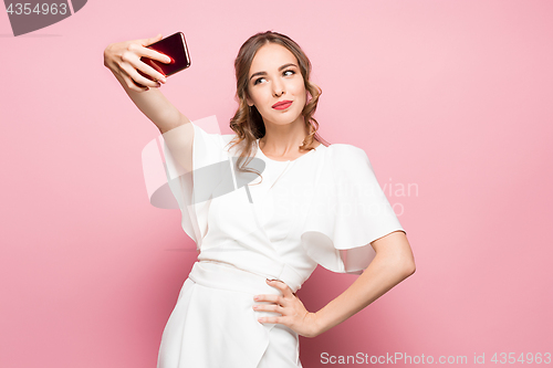 Image of Portrait of a young attractive woman making selfie photo with smartphone on a pink background