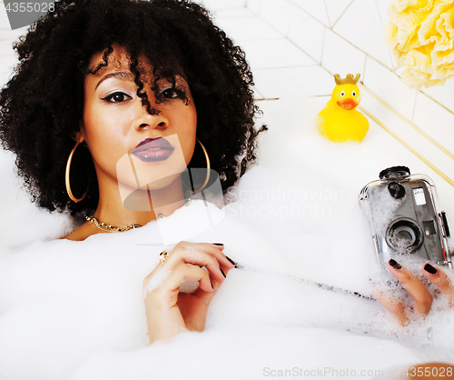 Image of young afro-american teen girl laying in bath with foam, wearing 