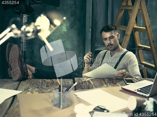Image of Portrait of a bearded businessman who is checking details of his upcoming meeting in his notebook and typing.