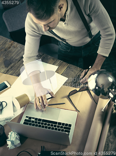 Image of Vintage hipster wooden desktop top view, male hands using a laptop and holding a pencil