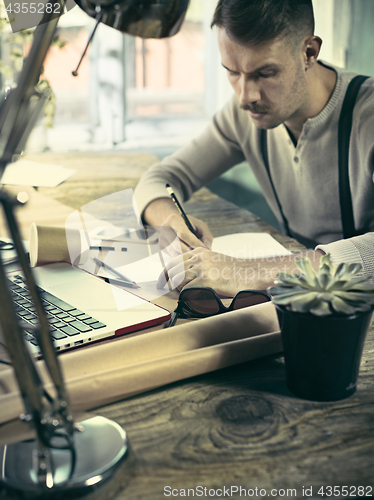 Image of Portrait of a bearded businessman who is checking details of his upcoming meeting in his notebook and typing.