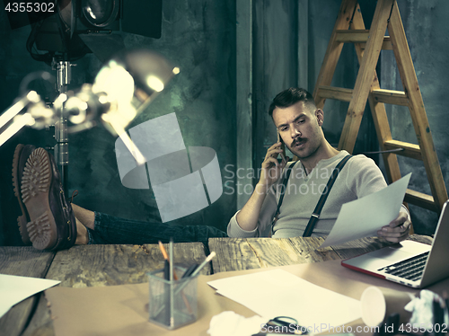 Image of Portrait of a bearded businessman who is working with his notebook at loft studio.