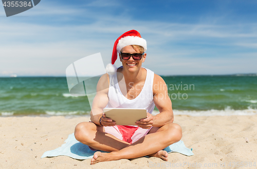 Image of happy man with tablet pc on beach at christmas