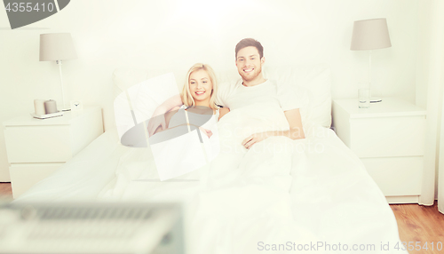 Image of happy couple lying in bed at home and watching tv