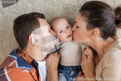 Image of happy family lying on floor and kissing their baby