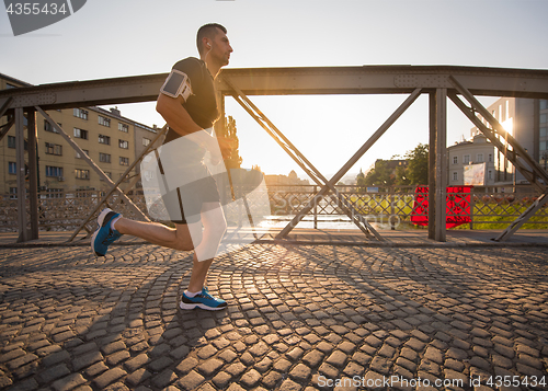 Image of man jogging across the bridge at sunny morning