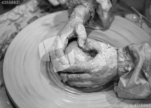 Image of Black and white hands of young girl in process of making clay bo