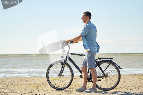Image of happy young man with bicycle on beach 