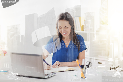 Image of happy woman writing to notebook at office