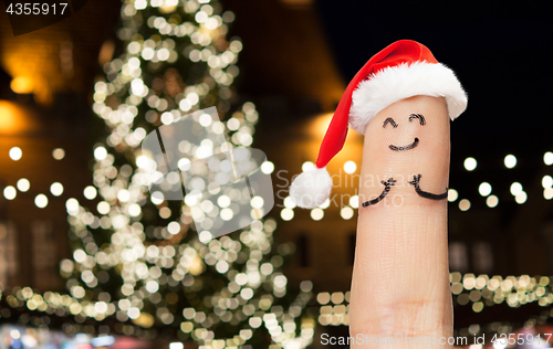 Image of finger with smiley in santa hat at christmas tree