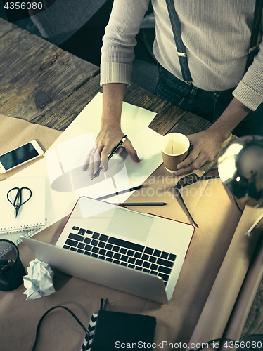 Image of Vintage hipster wooden desktop top view, male hands using a laptop and holding a pencil