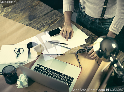 Image of Vintage hipster wooden desktop top view, male hands using a laptop and holding a pencil