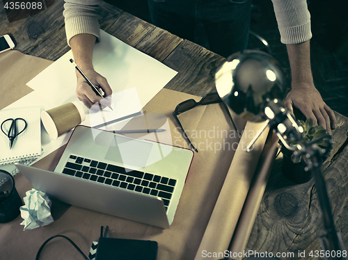 Image of Vintage hipster wooden desktop top view, male hands using a laptop and holding a pencil
