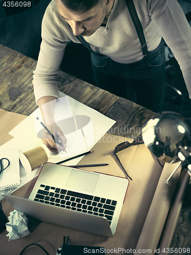 Image of Vintage hipster wooden desktop top view, male hands using a laptop and holding a pencil