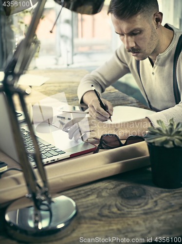 Image of Portrait of a bearded businessman who is checking details of his upcoming meeting in his notebook and typing.