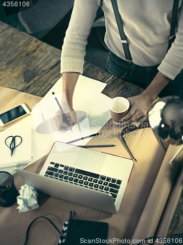 Image of Vintage hipster wooden desktop top view, male hands using a laptop and holding a pencil