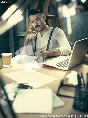 Image of Portrait of a bearded businessman who is checking details of his upcoming meeting in his notebook and typing.