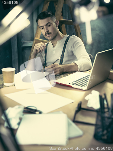 Image of Portrait of a bearded businessman who is checking details of his upcoming meeting in his notebook and typing.