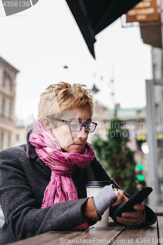 Image of Woman browsing smartphone in outside cafe
