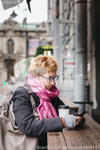 Image of Woman browsing smartphone in outside cafe