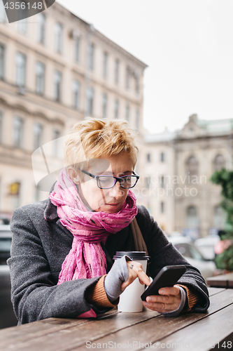 Image of Woman browsing smartphone in outside cafe