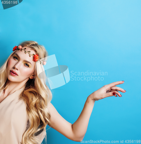 Image of young pretty blond girl with curly blond hair and little flowers happy smiling on blue sky background, lifestyle people concept closeup