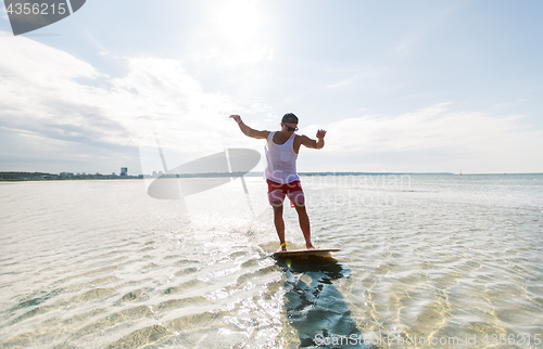 Image of young man riding on skimboard on summer beach