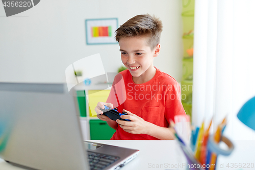 Image of boy with gamepad playing video game on laptop