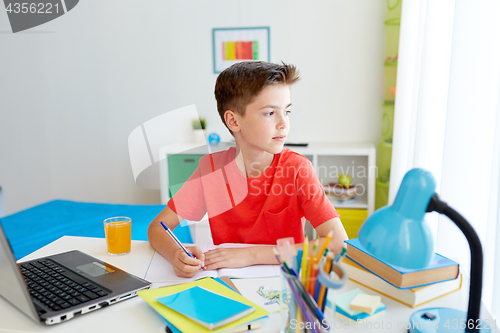 Image of student boy with laptop writing to notebook