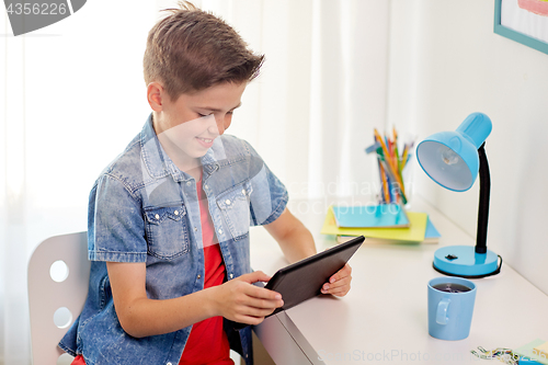 Image of smiling boy with tablet pc sitting at home desk