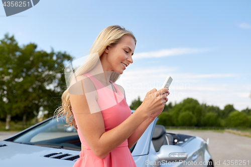 Image of young woman with smartphone at convertible car