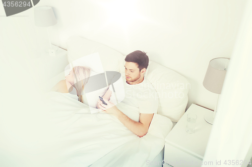 Image of man texting message while woman is sleeping in bed