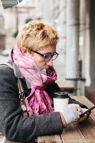 Image of Woman browsing smartphone in outside cafe