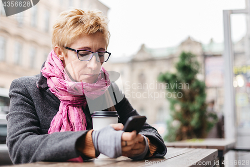 Image of Woman browsing phone in outside cafe