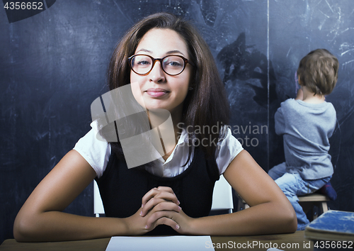 Image of little cute boy in glasses with young real teacher, classroom studying at blackboard school