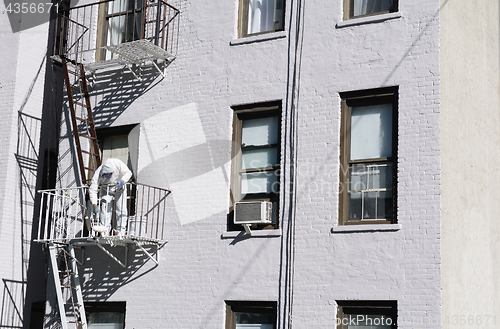 Image of Painter dressed in coveralls, painting metal fire escape white 