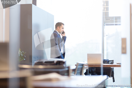 Image of Businessman talking on a mobile phone while looking through window.