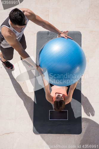 Image of woman and personal trainer doing exercise with pilates ball