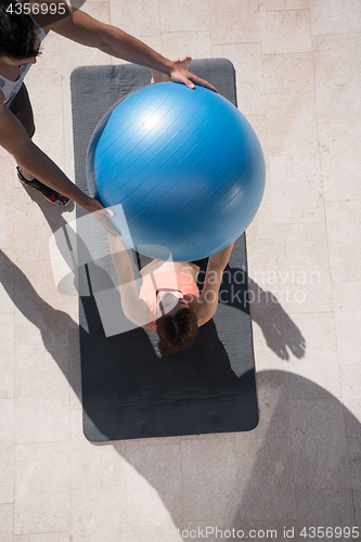 Image of woman and personal trainer doing exercise with pilates ball