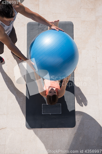 Image of woman and personal trainer doing exercise with pilates ball