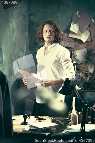 Image of Writer at work. Handsome young writer standing near the table and making up something in his mind