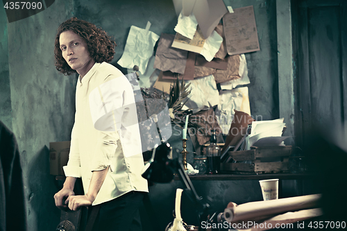 Image of Writer at work. Handsome young writer standing near the table and making up something in his mind