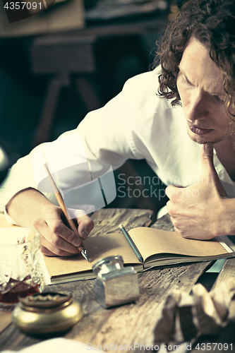 Image of Writer at work. Handsome young writer sitting at the table and writing something in his sketchpad