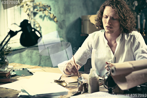 Image of Writer at work. Handsome young writer sitting at the table and writing something in his sketchpad