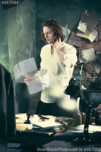 Image of Writer at work. Handsome young writer standing near the table and making up something in his mind