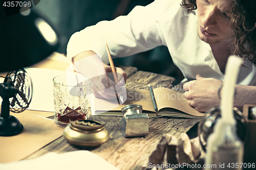 Image of Writer at work. Handsome young writer sitting at the table and writing something in his sketchpad